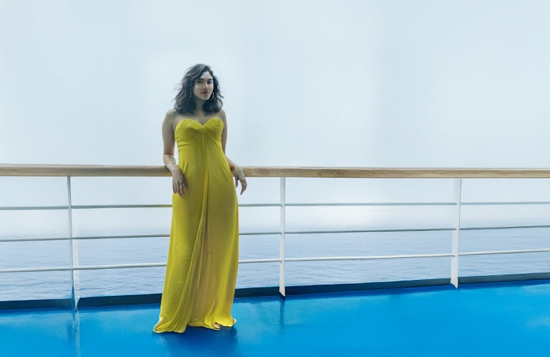 Woman in yellow dress poses on a cruise deck.