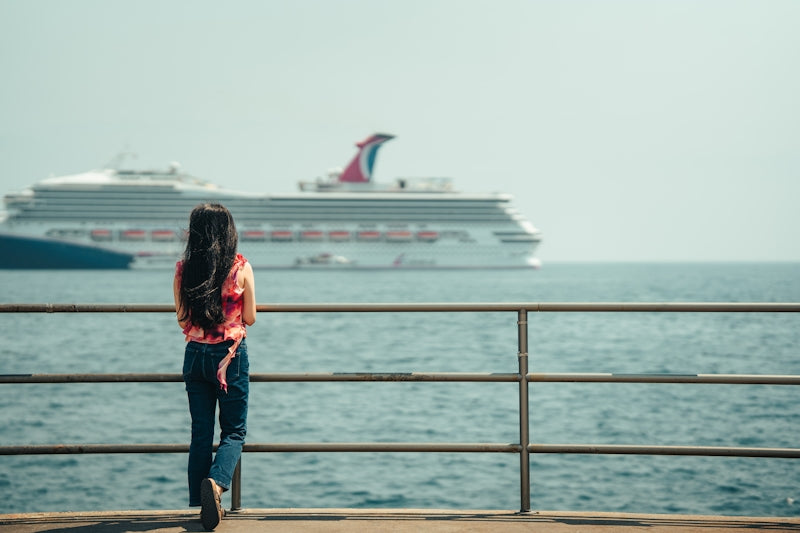 Woman watches a large cruise ship on the ocean.